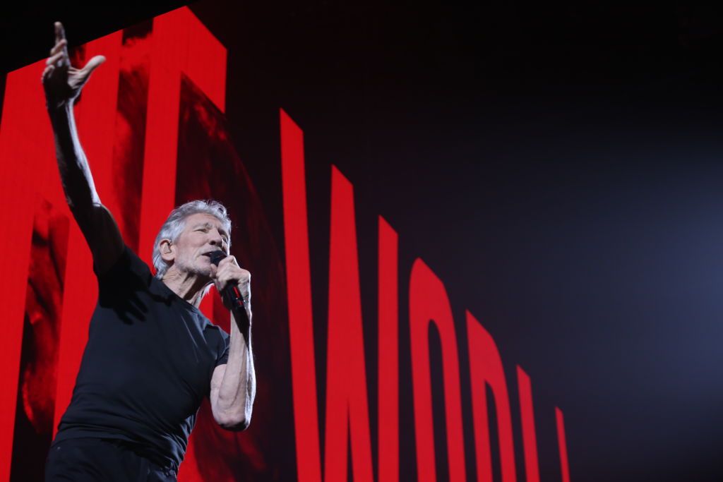 Roger Waters performing in front of a red sign