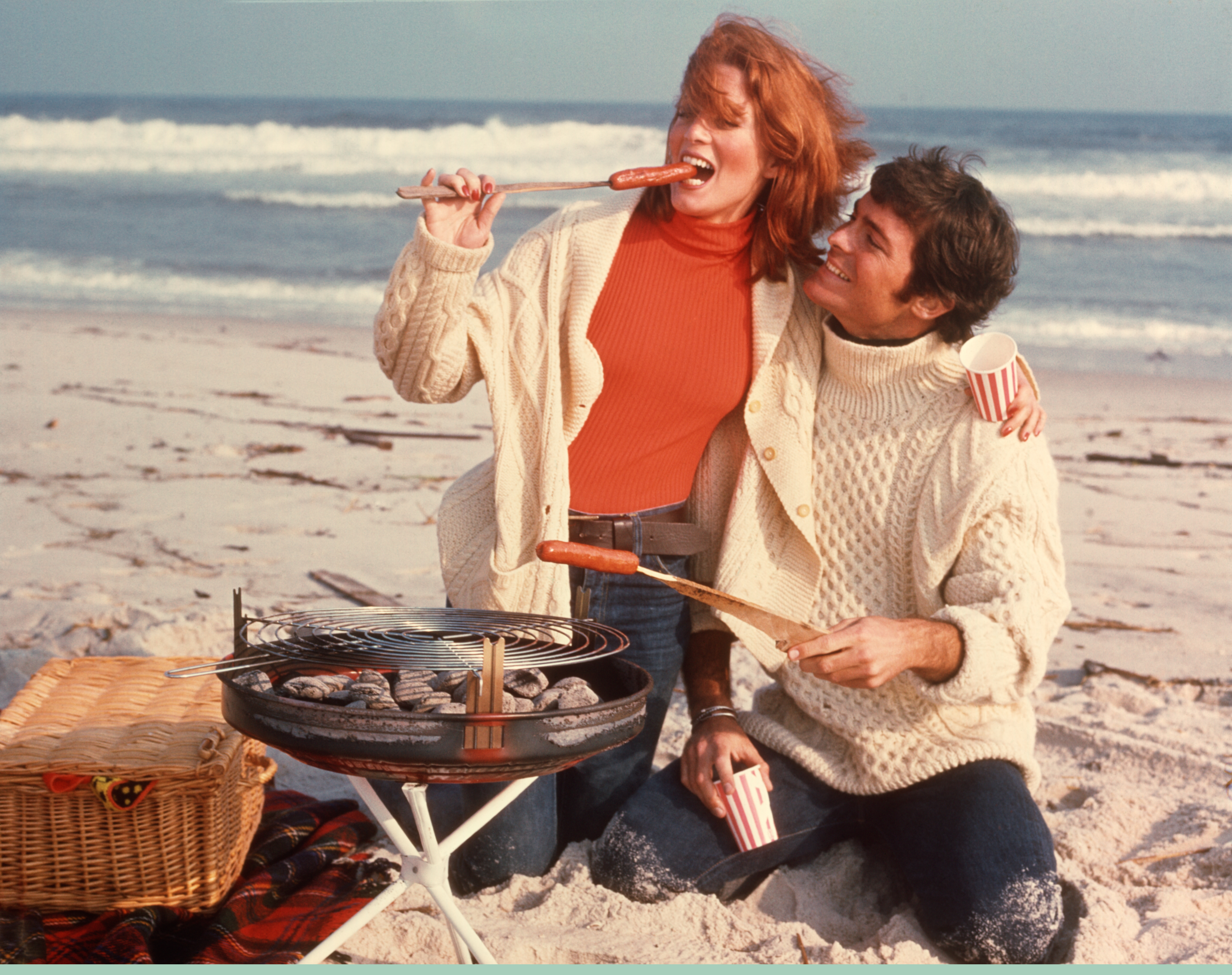 A couple eating hot dogs outside on the beach.