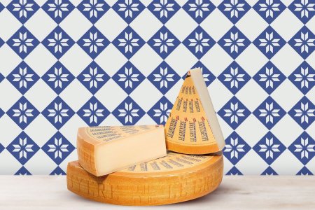 a wheel of gruyere cheese with two wedges on top of it sitting in front of a blue and white tiled wall