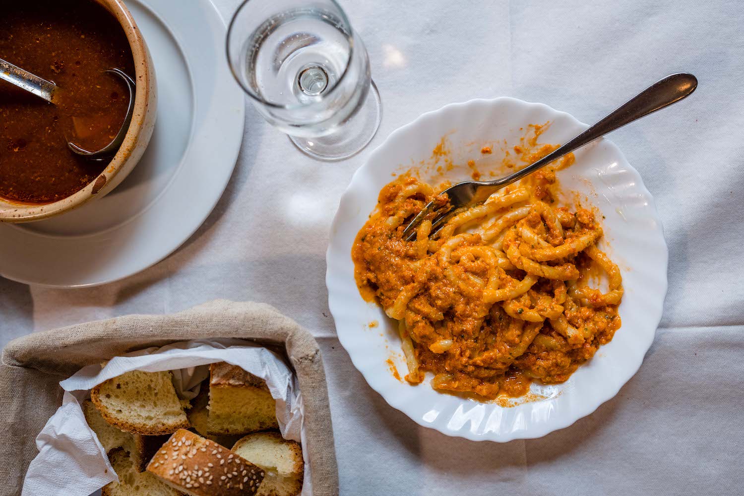 Pasta Cu L'Agghia sitting next to a bread basket, goblet of water and sauce