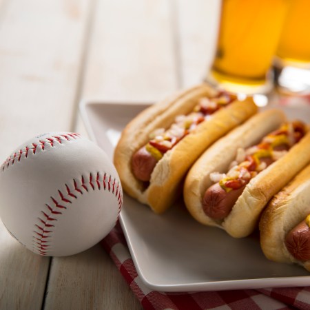 Three hot dogs on a white plate on a white wooden picnic bench