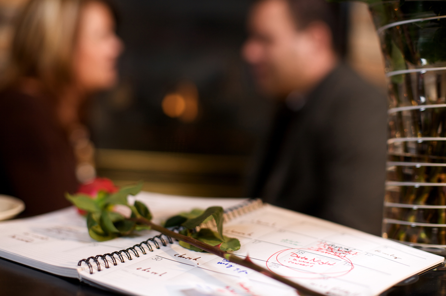 man and woman in background with red rose and calendar showing date night