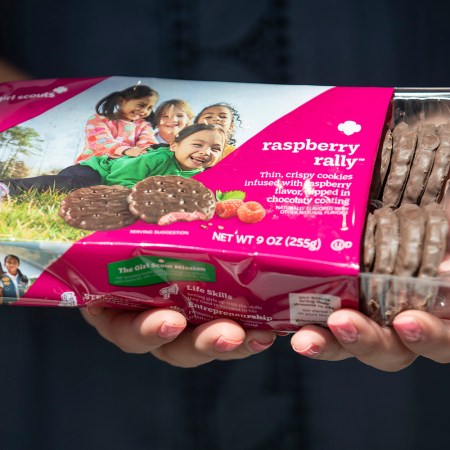 a girl scout holding a box of Raspberry Rally cookies