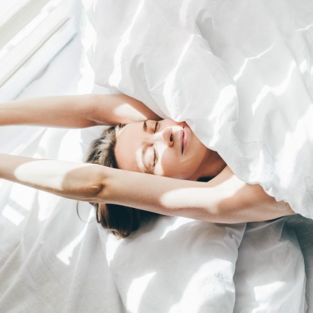 top view of a woman sleeping under a white duvet on a sunny morning