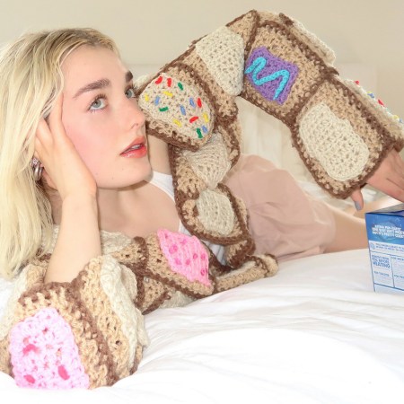 A woman wearing the Pop-Tarts Pop-Tartigan sitting next to a box of the new Frosted Banana Bread flavor