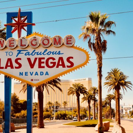 The famous "Welcome to Las Vegas" sign stands between palm trees under a cloudless sky