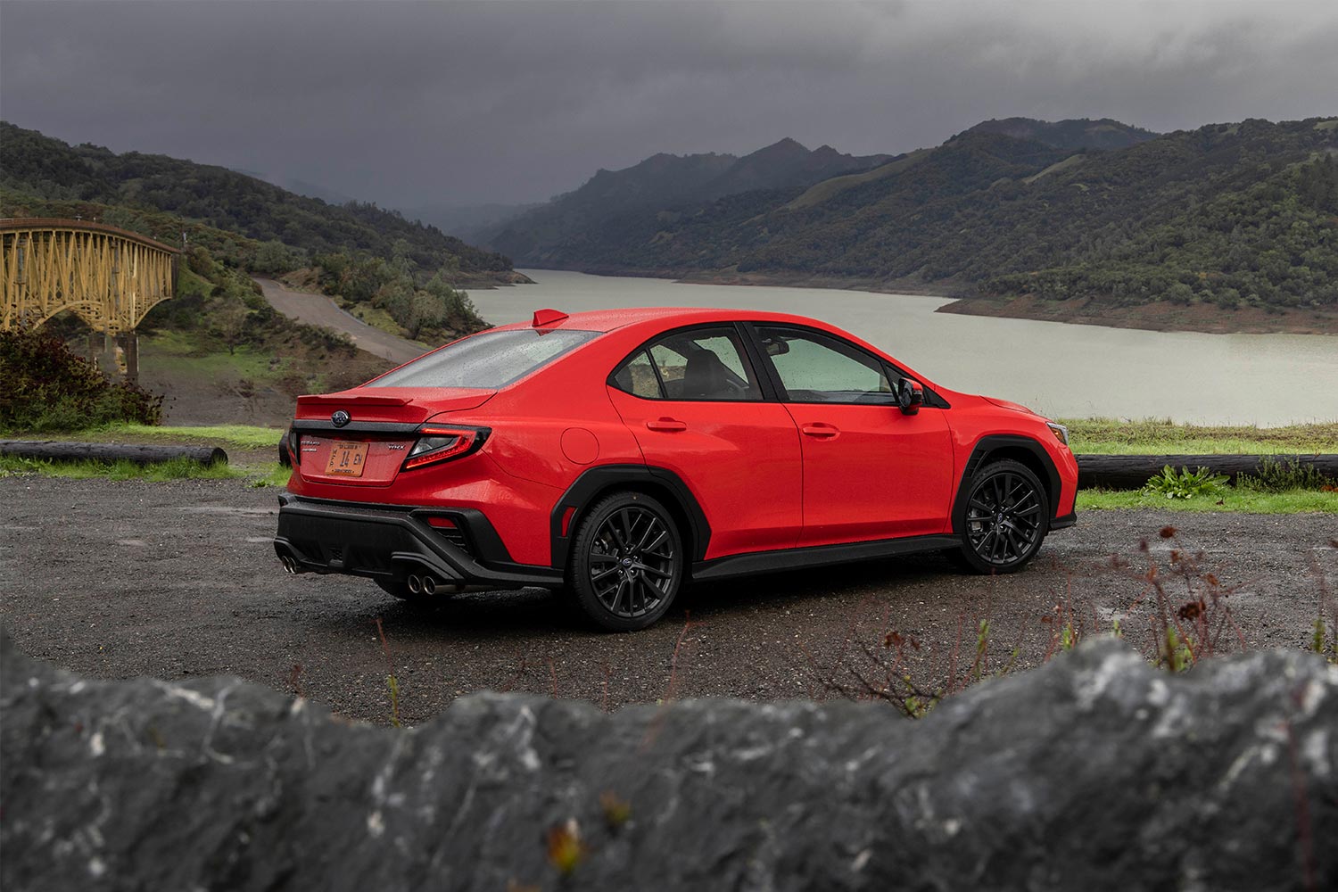 A red Subaru WRX performance car sitting on the road overlooking a lake and hills