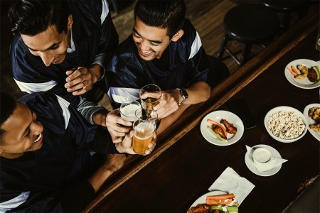 High angle view of excited sports fans toasting beer glasses at counter in bar