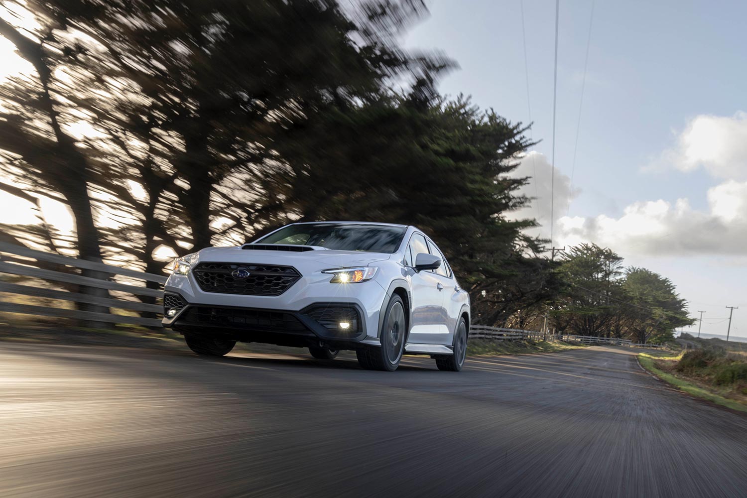 A white 2023 Subaru WRX speeding down a road. We tested and reviewed the high performance sedan.